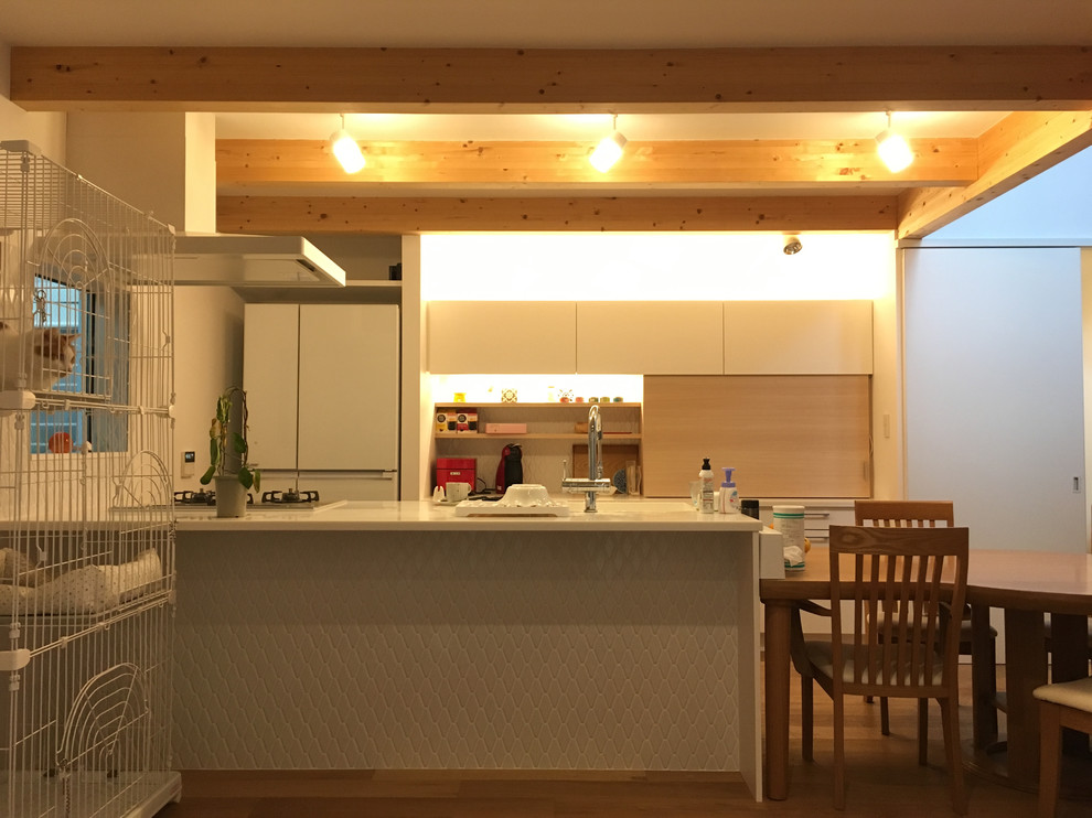 東京都下にあるシャビーシック調のおしゃれなキッチン (一体型シンク、フラットパネル扉のキャビネット、白いキャビネット、人工大理石カウンター、白いキッチンパネル、セラミックタイルのキッチンパネル、シルバーの調理設備、無垢フローリング、茶色い床、白いキッチンカウンター) の写真