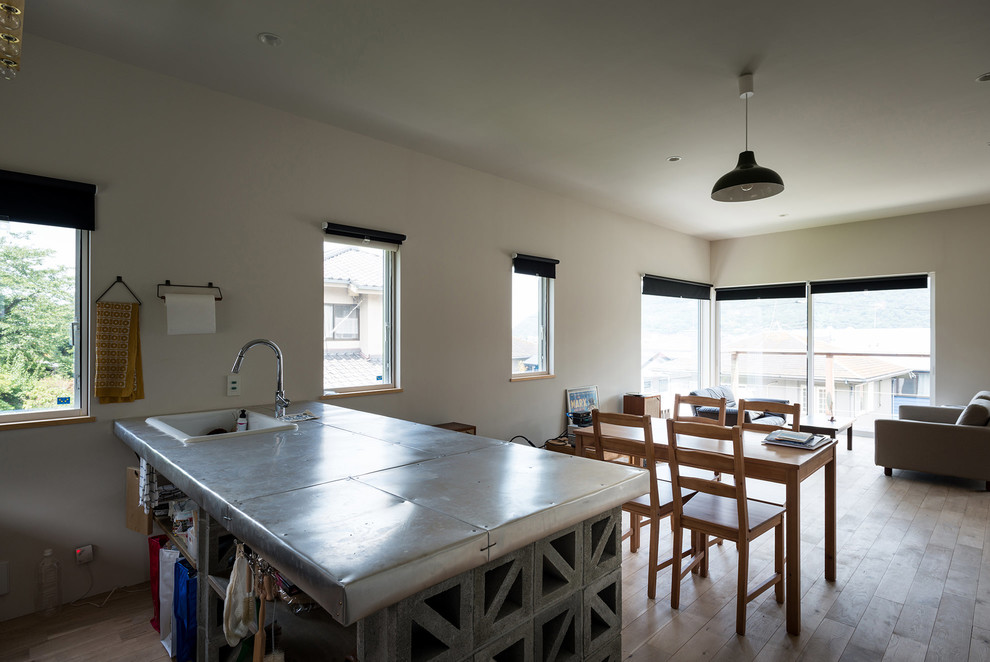 Foto på ett maritimt kök med öppen planlösning, med en nedsänkt diskho, öppna hyllor, grå skåp, ljust trägolv och en halv köksö