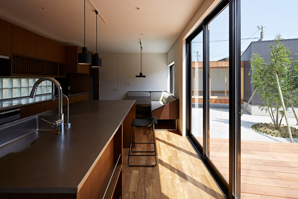 Offene Retro Küche mit integriertem Waschbecken, flächenbündigen Schrankfronten, hellbraunen Holzschränken, Glasrückwand, Kücheninsel und braunem Holzboden in Sonstige