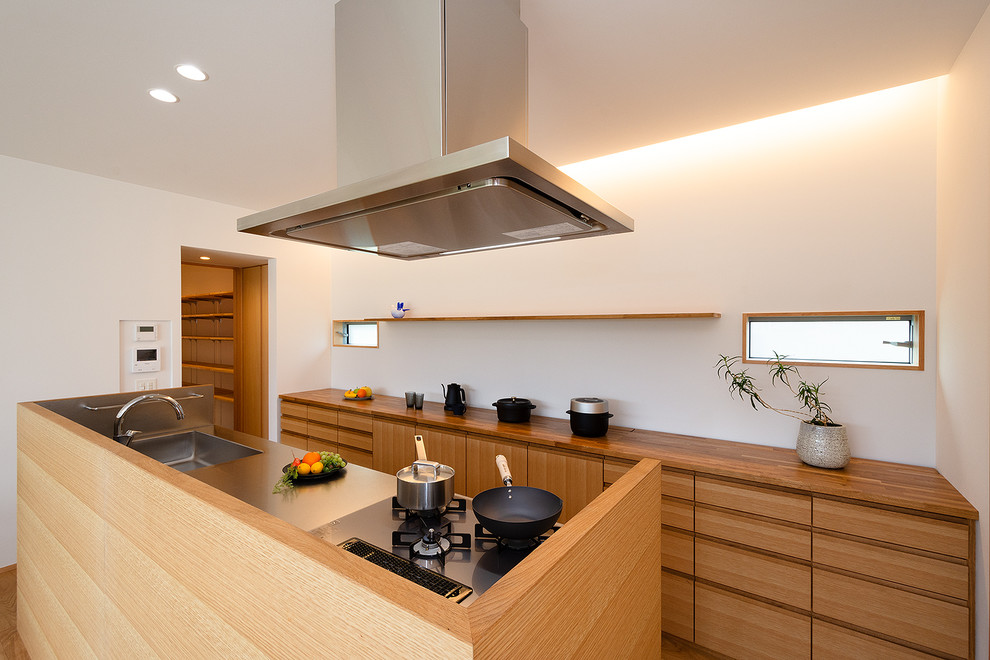 Inspiration för stora minimalistiska linjära brunt kök med öppen planlösning, med brunt golv, släta luckor, en integrerad diskho, skåp i mellenmörkt trä, bänkskiva i rostfritt stål, stänkskydd med metallisk yta, svarta vitvaror, mellanmörkt trägolv och en köksö