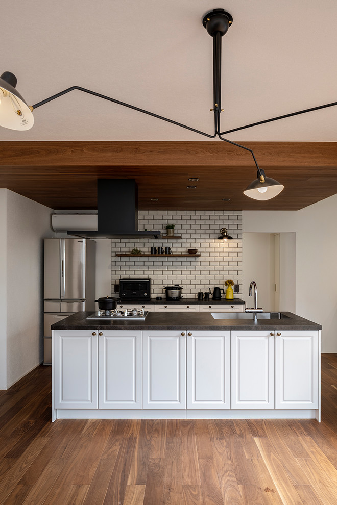 Immagine di una cucina industriale con lavello sottopiano, ante a filo, ante bianche, elettrodomestici neri, pavimento in legno massello medio, pavimento marrone e top nero