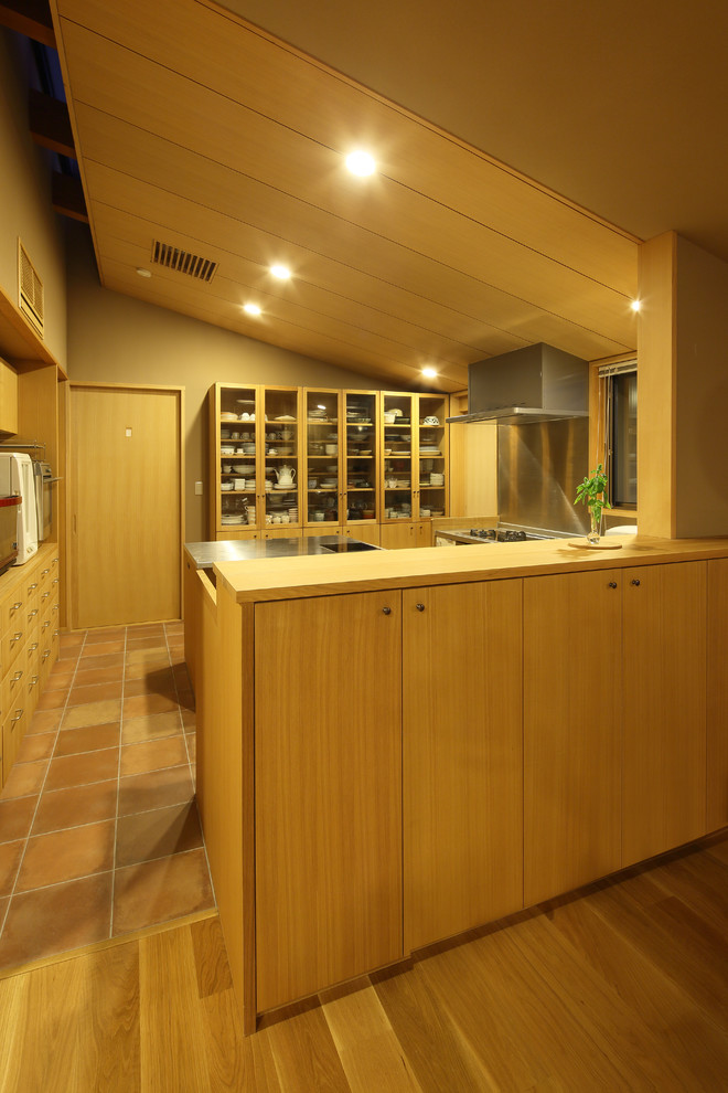 京都にあるアジアンスタイルのおしゃれなキッチン (フラットパネル扉のキャビネット、淡色木目調キャビネット、ステンレスカウンター、メタリックのキッチンパネル、シルバーの調理設備、テラコッタタイルの床) の写真