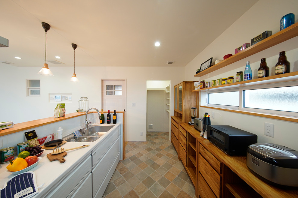 他の地域にあるカントリー風のおしゃれなキッチン (シングルシンク、フラットパネル扉のキャビネット、白いキャビネット、マルチカラーの床、茶色いキッチンカウンター) の写真