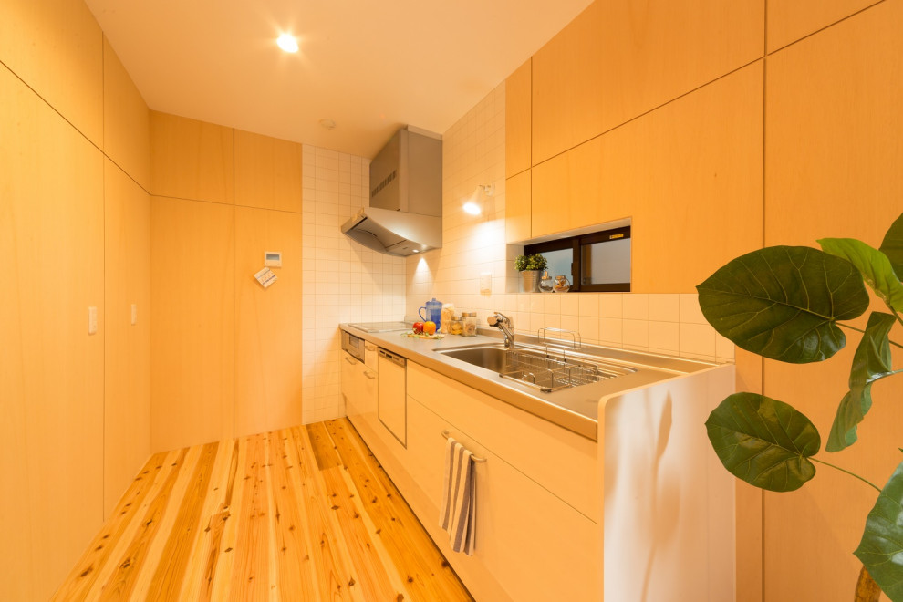 Bild på ett shabby chic-inspirerat linjärt kök med öppen planlösning, med släta luckor, vita skåp, bänkskiva i rostfritt stål, vitt stänkskydd, ljust trägolv och beiget golv