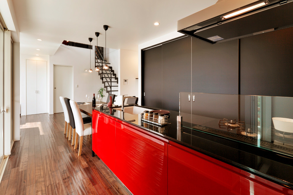 Réalisation d'une cuisine ouverte linéaire minimaliste avec un plan de travail en granite, un électroménager noir, un sol en bois brun et un sol marron.