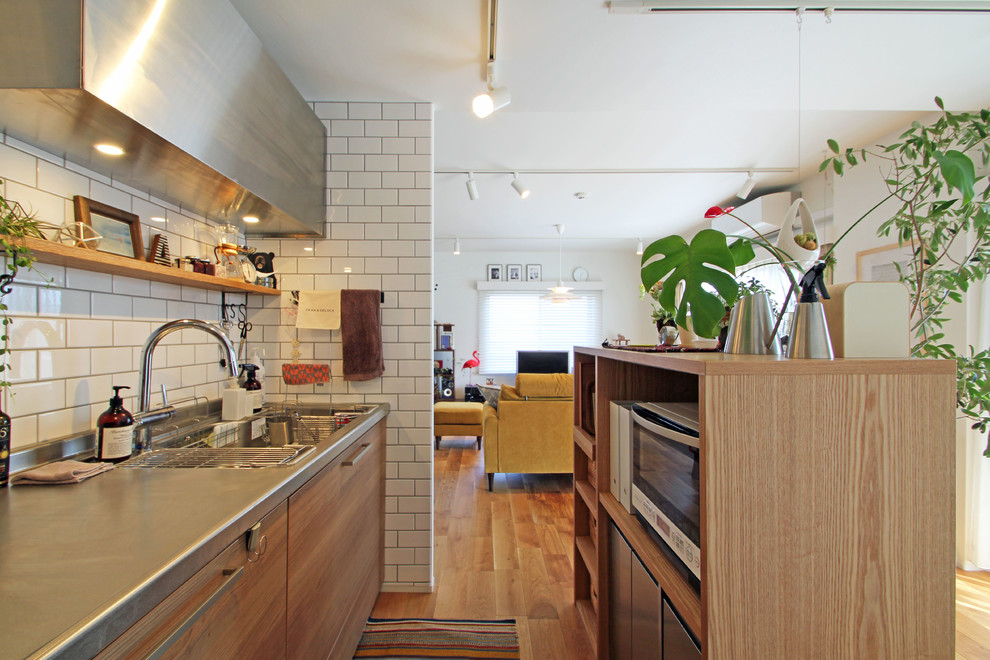 Kleine Asiatische Küche mit integriertem Waschbecken, flächenbündigen Schrankfronten, hellbraunen Holzschränken, Küchenrückwand in Weiß, Rückwand aus Metrofliesen und braunem Holzboden in Yokohama