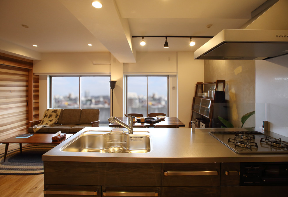 Inspiration pour une cuisine ouverte linéaire minimaliste de taille moyenne avec un plan de travail en inox et un sol en bois brun.