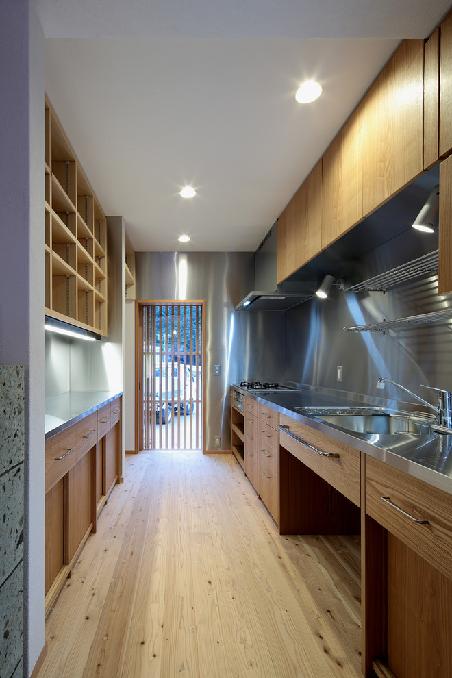 Idée de décoration pour une cuisine parallèle nordique en bois brun fermée avec un évier intégré, un placard à porte affleurante, un plan de travail en inox, une crédence métallisée, un électroménager en acier inoxydable, parquet clair et un sol beige.