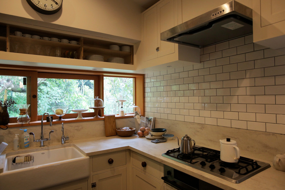 東京都下にあるビーチスタイルのおしゃれなキッチン (エプロンフロントシンク、インセット扉のキャビネット、白いキャビネット、白いキッチンパネル、サブウェイタイルのキッチンパネル、シルバーの調理設備、人工大理石カウンター、リノリウムの床、グレーの床、白いキッチンカウンター) の写真