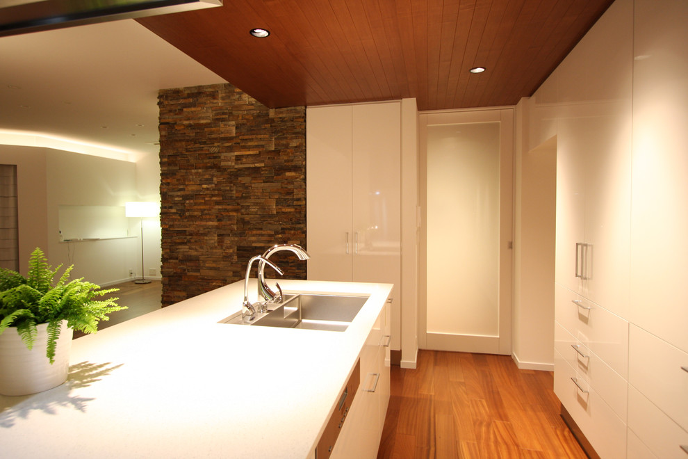 This is an example of a medium sized contemporary galley open plan kitchen in Tokyo with a submerged sink, flat-panel cabinets, white cabinets, engineered stone countertops, white splashback, stainless steel appliances, plywood flooring, an island and brown floors.