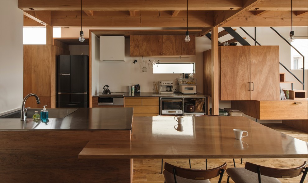 Small world-inspired galley open plan kitchen in Other with an integrated sink, beige cabinets, stainless steel worktops, white splashback, ceramic splashback, stainless steel appliances, medium hardwood flooring, an island, beige floors, grey worktops and flat-panel cabinets.