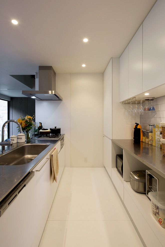 Moderne Küche mit Waschbecken, flächenbündigen Schrankfronten, weißen Schränken, Edelstahl-Arbeitsplatte, Küchenrückwand in Weiß und weißem Boden in Sonstige