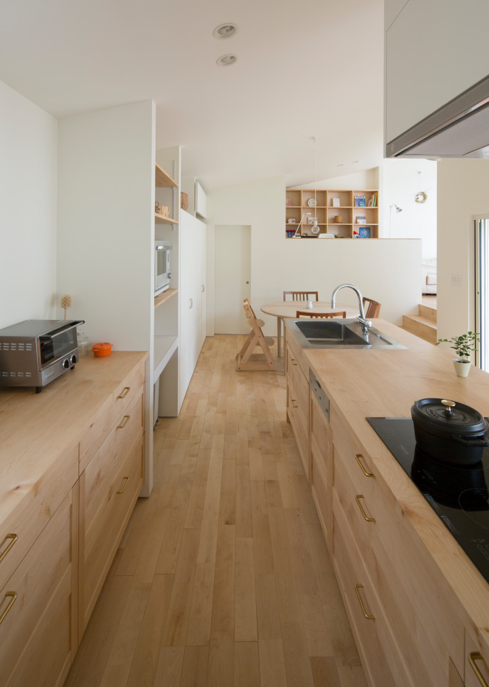 Photo of a medium sized world-inspired galley open plan kitchen in Nagoya with a built-in sink, light wood cabinets, wood worktops, stainless steel appliances, light hardwood flooring, an island, brown floors, beige worktops, shaker cabinets, white splashback and tonge and groove splashback.