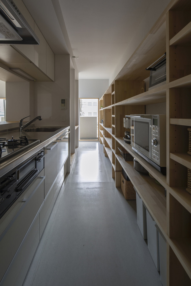 Foto på ett avskilt, mellanstort funkis brun linjärt kök, med en enkel diskho, luckor med profilerade fronter, vita skåp, bänkskiva i rostfritt stål, vitt stänkskydd, rostfria vitvaror, en köksö, glaspanel som stänkskydd, ljust trägolv och grått golv
