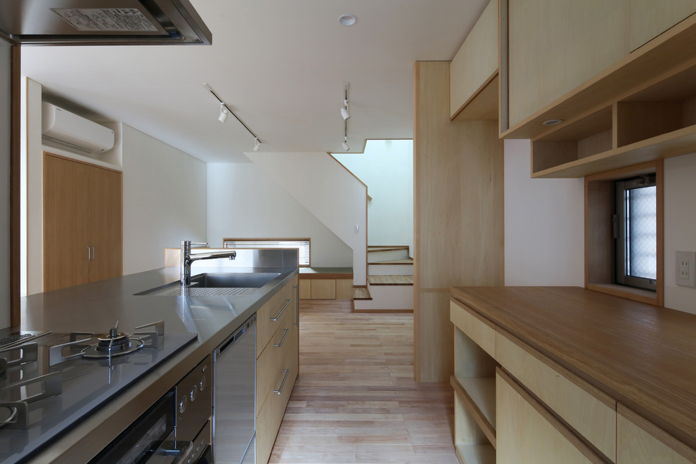This is an example of a medium sized modern single-wall open plan kitchen in Tokyo with an integrated sink, beige cabinets, stainless steel worktops, white splashback, integrated appliances, light hardwood flooring, a breakfast bar, beige floors, flat-panel cabinets, glass sheet splashback and beige worktops.