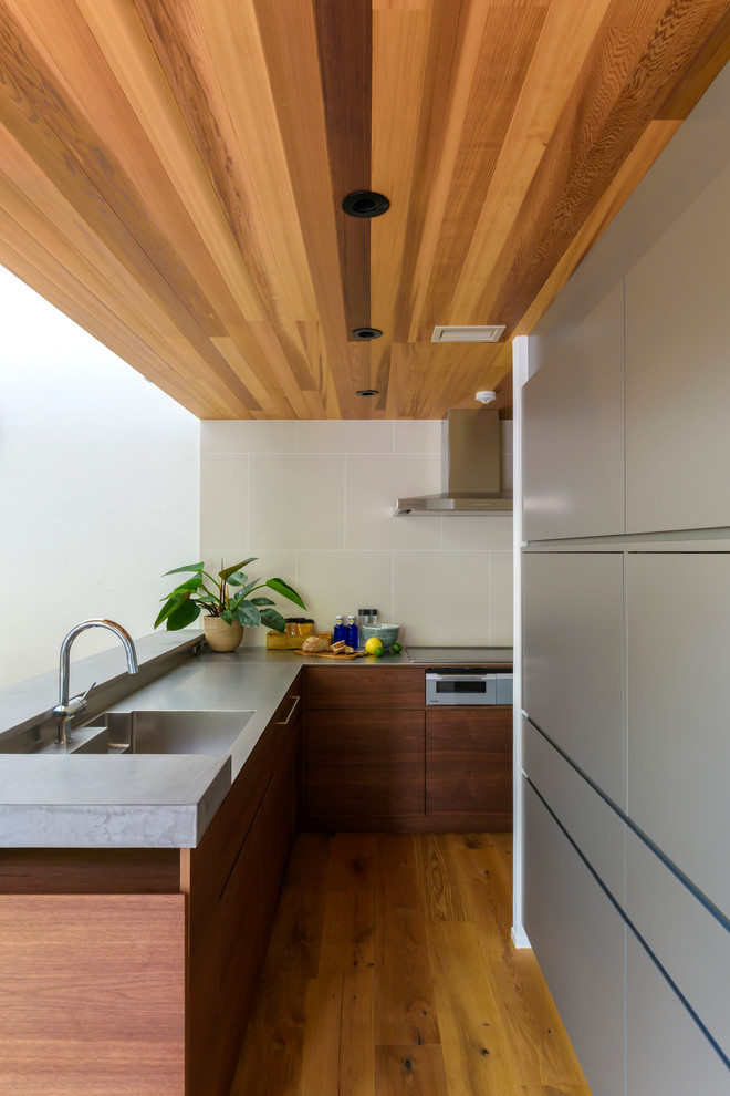 Modern inredning av ett grå grått l-kök, med en integrerad diskho, släta luckor, skåp i mörkt trä, bänkskiva i rostfritt stål, mellanmörkt trägolv, en halv köksö och brunt golv