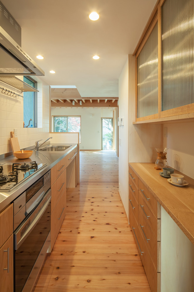 This is an example of a small modern single-wall open plan kitchen in Tokyo with a single-bowl sink, flat-panel cabinets, medium wood cabinets, stainless steel worktops, white splashback, porcelain splashback, stainless steel appliances, medium hardwood flooring, an island and brown floors.