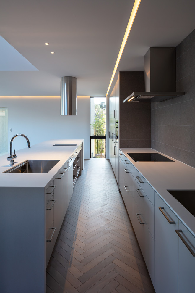 Свежая идея для дизайна: параллельная кухня в стиле модернизм с одинарной мойкой, плоскими фасадами, серыми фасадами, деревянным полом, островом, серым полом и белой столешницей - отличное фото интерьера