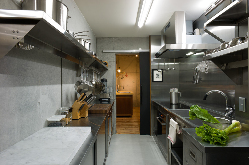 Cette photo montre une cuisine parallèle industrielle en inox fermée avec un évier 2 bacs, un placard à porte plane, un plan de travail en inox, une crédence métallisée, sol en béton ciré, aucun îlot et un sol gris.