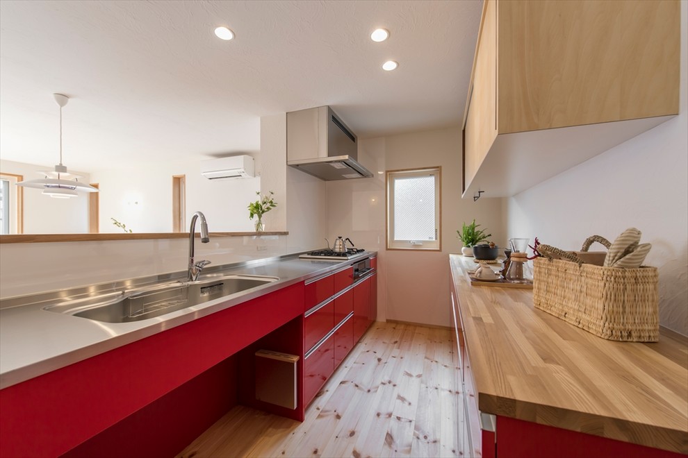 Idéer för nordiska brunt kök, med en enkel diskho, släta luckor, röda skåp, bänkskiva i rostfritt stål, mellanmörkt trägolv, en halv köksö och brunt golv