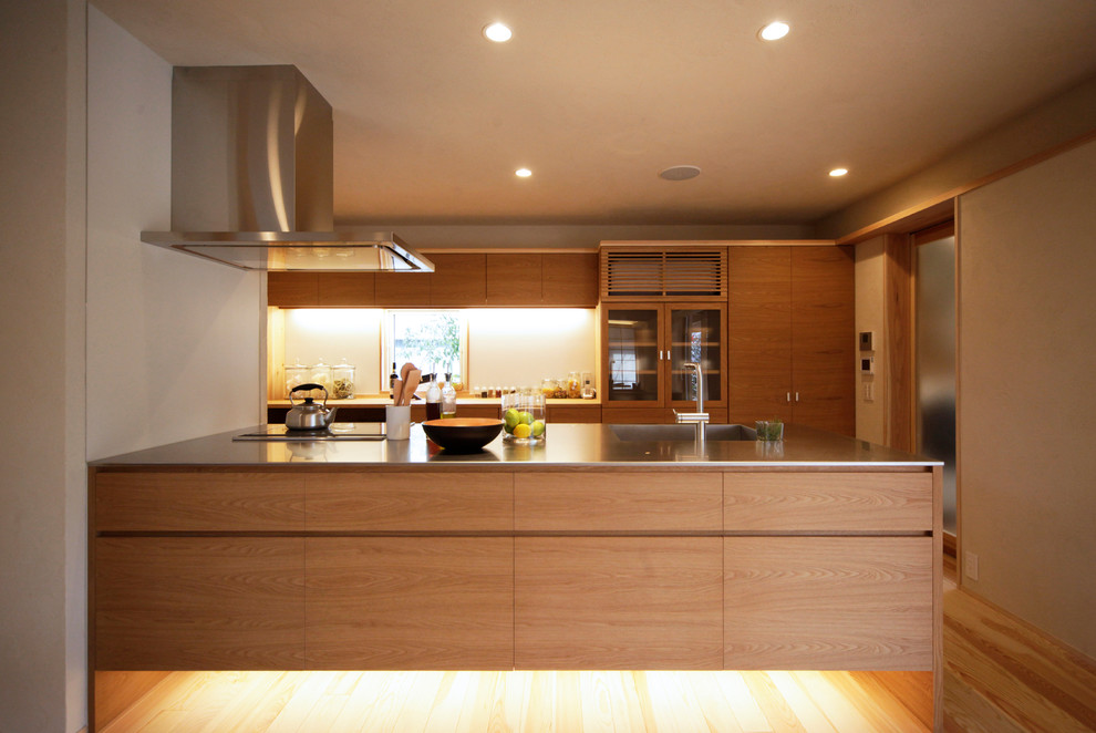 Asiatisk inredning av ett kök med öppen planlösning, med en enkel diskho, släta luckor, skåp i mellenmörkt trä, bänkskiva i rostfritt stål, mellanmörkt trägolv, en halv köksö och brunt golv