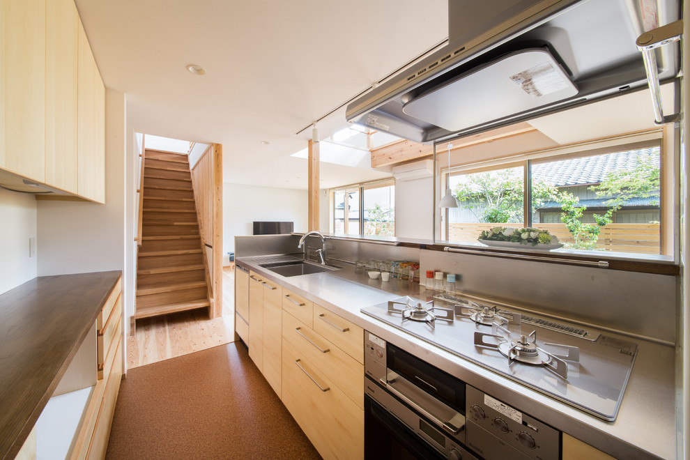 This is an example of a world-inspired kitchen in Other with an integrated sink, flat-panel cabinets, light wood cabinets, stainless steel worktops, metallic splashback, an island and brown floors.