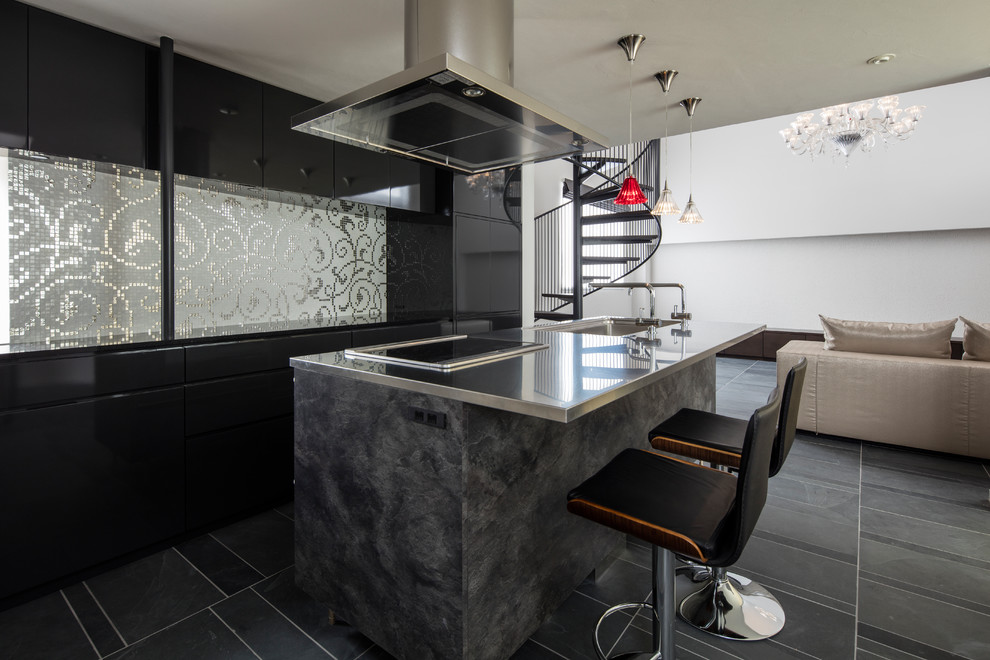 Imagen de cocina lineal actual grande abierta con puertas de armario negras, encimera de acero inoxidable, salpicadero negro, una isla y suelo negro