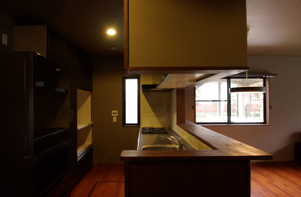 Foto på ett litet orientaliskt brun linjärt kök med öppen planlösning, med en integrerad diskho, luckor med profilerade fronter, skåp i mörkt trä, bänkskiva i rostfritt stål, rosa stänkskydd, stänkskydd i keramik, rostfria vitvaror, mörkt trägolv, en köksö och brunt golv