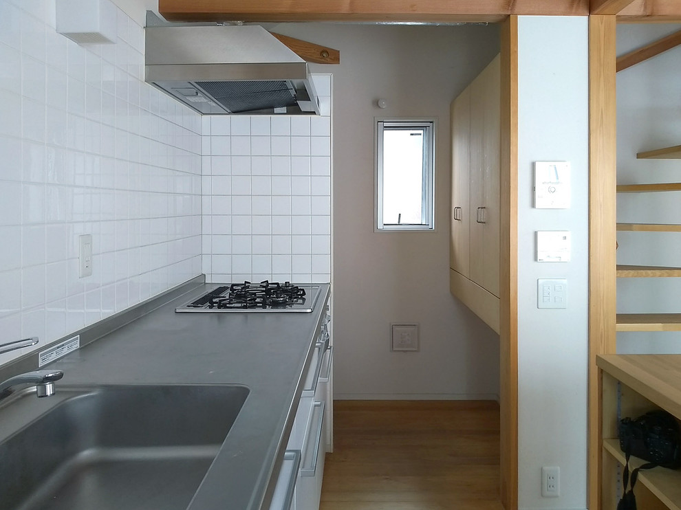 Exempel på ett nordiskt linjärt kök, med bänkskiva i rostfritt stål, vitt stänkskydd och en köksö