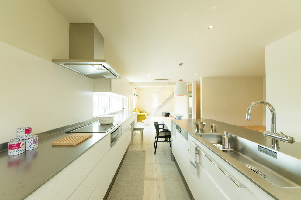 Esempio di una cucina parallela scandinava con lavello integrato, ante lisce, ante bianche, top in acciaio inossidabile e pavimento beige