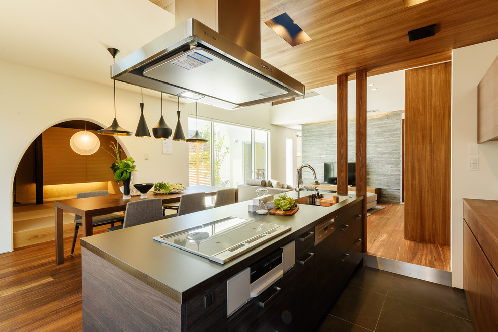 Cette photo montre une cuisine ouverte parallèle asiatique en bois brun avec un évier intégré, un placard à porte plane, îlot et un sol noir.