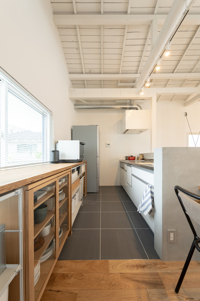 Example of a zen single-wall gray floor open concept kitchen design in Other with flat-panel cabinets, white cabinets, stainless steel countertops and a peninsula