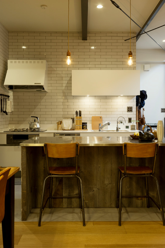 Imagen de cocina urbana abierta con salpicadero blanco, salpicadero de azulejos tipo metro, suelo de madera en tonos medios, una isla y suelo marrón