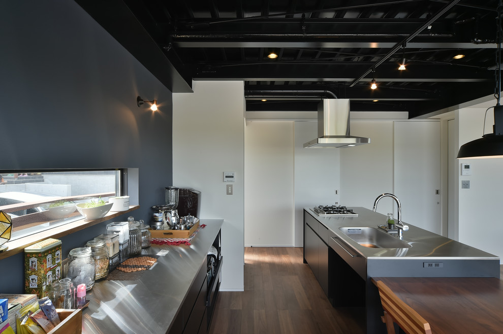 Exempel på ett industriellt linjärt kök, med bänkskiva i rostfritt stål, en enkel diskho, släta luckor, skåp i mörkt trä, grått stänkskydd, mörkt trägolv, en köksö och brunt golv
