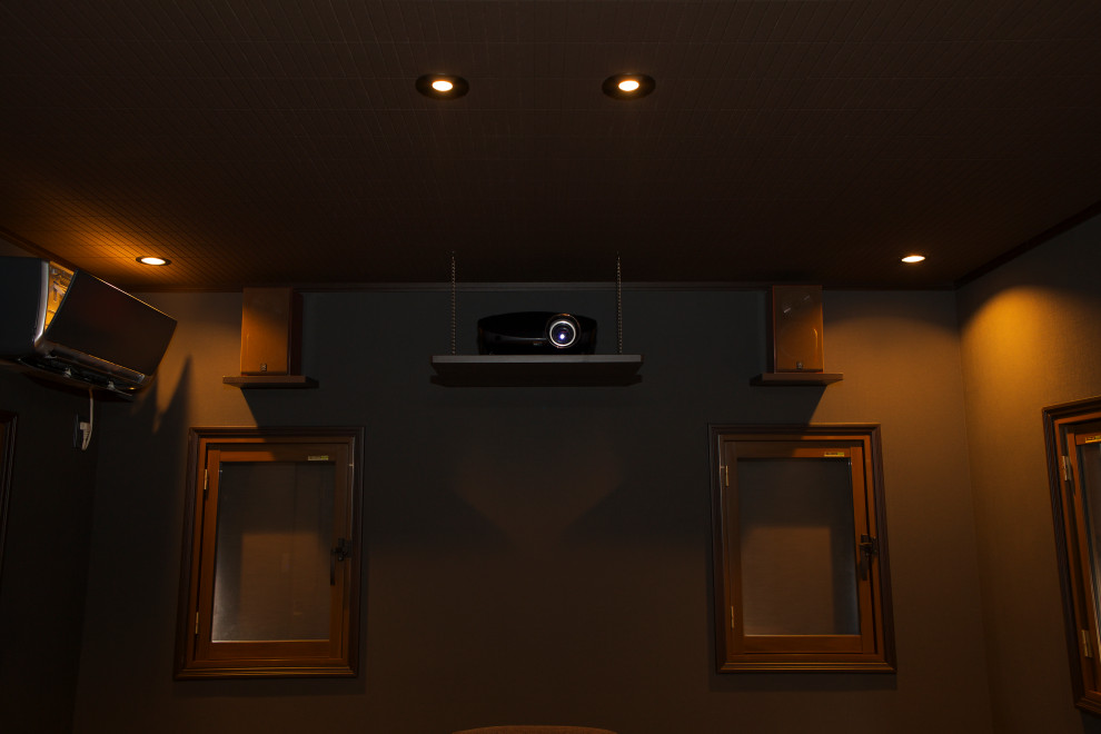 Cette image montre une salle de cinéma minimaliste avec un mur gris, parquet peint, un écran de projection et un sol marron.