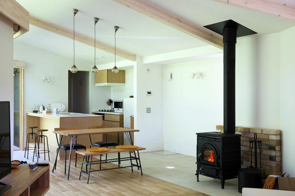 Idée de décoration pour une salle à manger ouverte sur le salon minimaliste avec un mur blanc, un poêle à bois, un manteau de cheminée en brique et un sol multicolore.