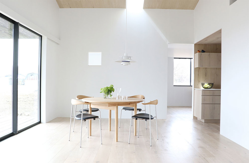 Cette image montre une salle à manger ouverte sur le salon nordique avec un mur blanc, parquet clair, un poêle à bois, un manteau de cheminée en bois et un sol blanc.