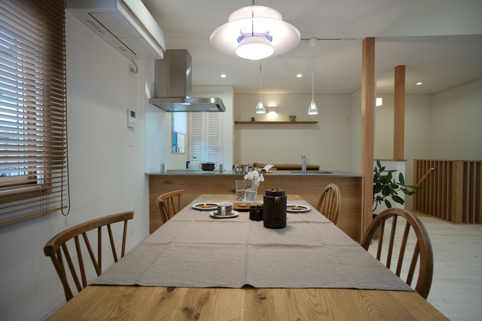 Immagine di una sala da pranzo aperta verso il soggiorno nordica con pareti bianche, parquet chiaro, nessun camino e pavimento bianco