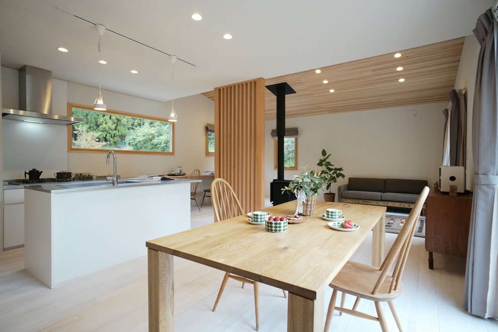 Inspiration pour une salle à manger ouverte sur le salon minimaliste avec un mur blanc, parquet clair, un poêle à bois, un manteau de cheminée en pierre et un sol blanc.