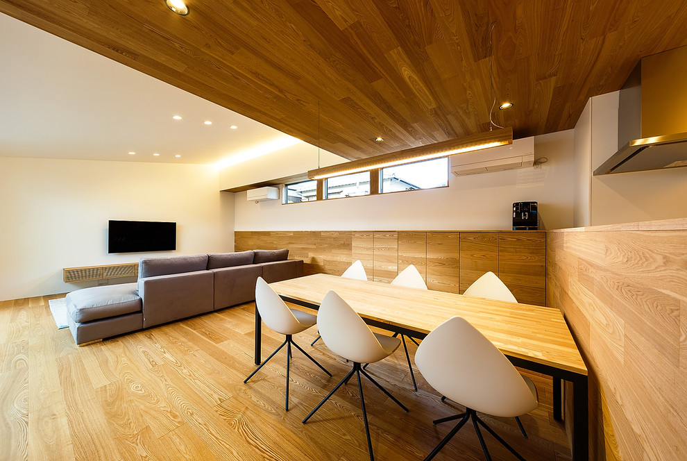 Idée de décoration pour une salle à manger ouverte sur le salon minimaliste de taille moyenne avec un mur blanc, un sol en contreplaqué et un sol marron.