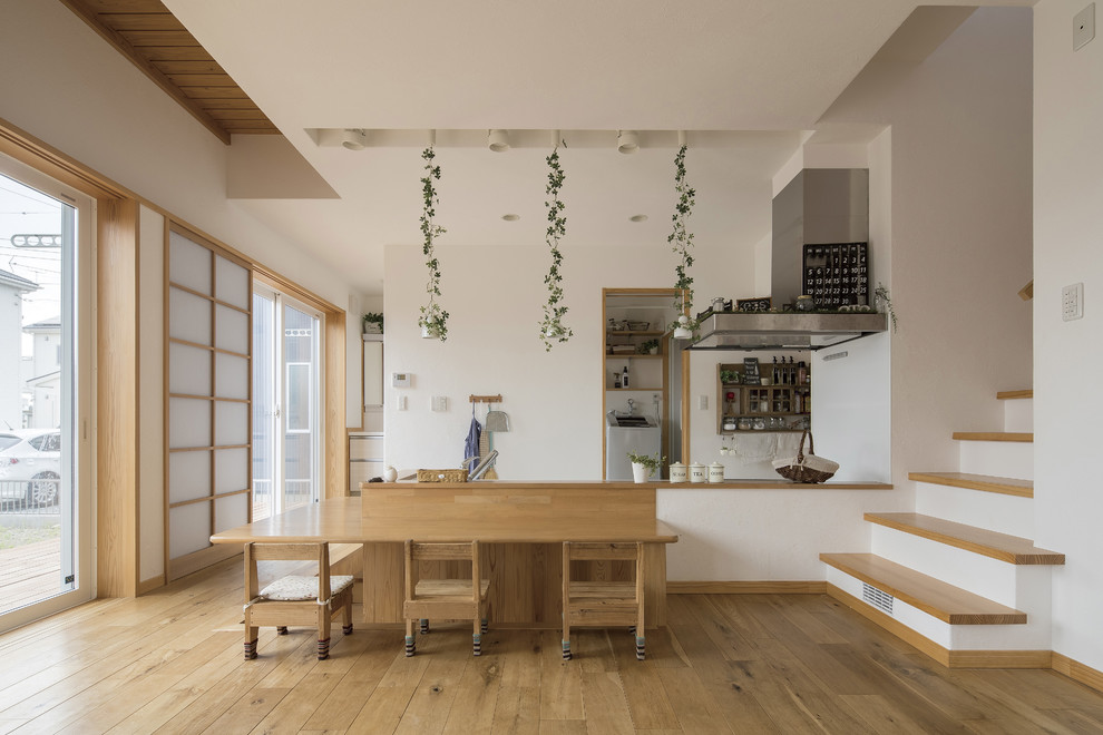 Foto di una sala da pranzo aperta verso il soggiorno nordica con pareti bianche, pavimento in legno massello medio, nessun camino e pavimento marrone