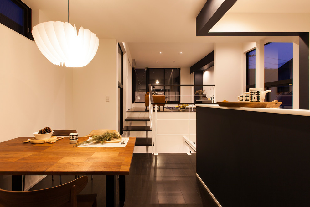 Esempio di una piccola sala da pranzo aperta verso la cucina minimalista con pareti bianche, pavimento in compensato e pavimento nero