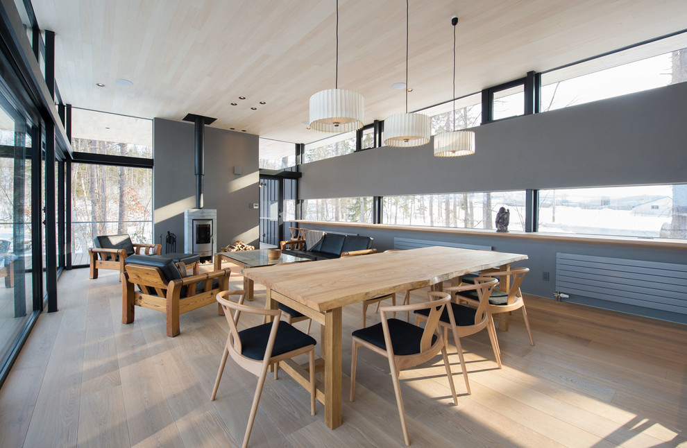 Foto di una sala da pranzo aperta verso il soggiorno minimalista con pareti grigie, pavimento in legno verniciato, stufa a legna e pavimento grigio