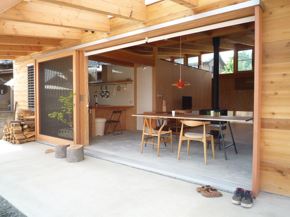 На фото: маленькая гостиная-столовая в восточном стиле с бетонным полом, печью-буржуйкой и фасадом камина из дерева для на участке и в саду