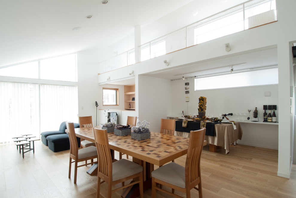 Cette image montre une salle à manger ouverte sur le salon minimaliste avec un mur blanc et parquet clair.