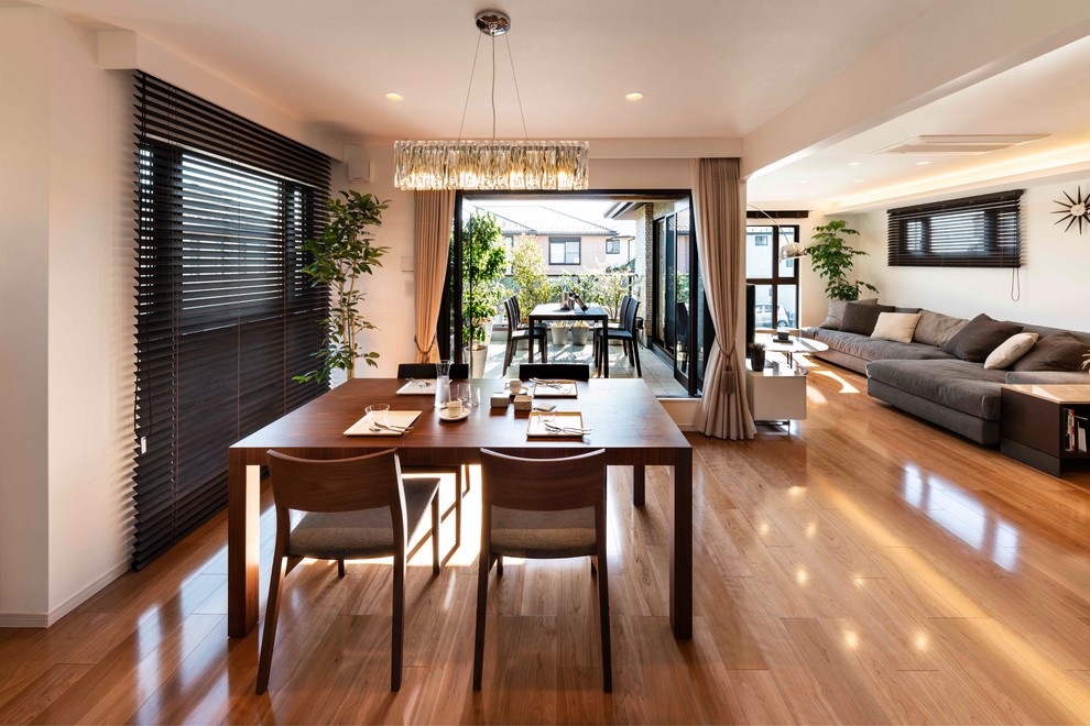 Immagine di una grande sala da pranzo aperta verso il soggiorno minimal con pareti bianche, pavimento in compensato e pavimento marrone