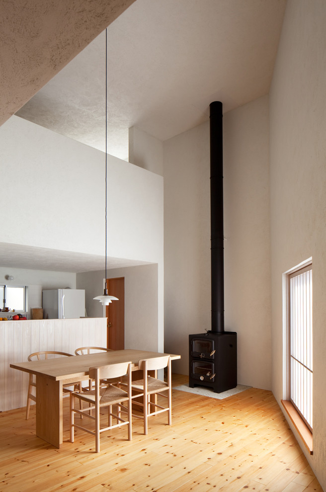Foto de comedor escandinavo con paredes blancas, suelo de madera en tonos medios, estufa de leña, marco de chimenea de piedra y suelo marrón