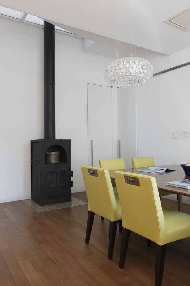 Réalisation d'une salle à manger minimaliste de taille moyenne avec un mur blanc, un sol en bois brun, un poêle à bois et un manteau de cheminée en pierre.