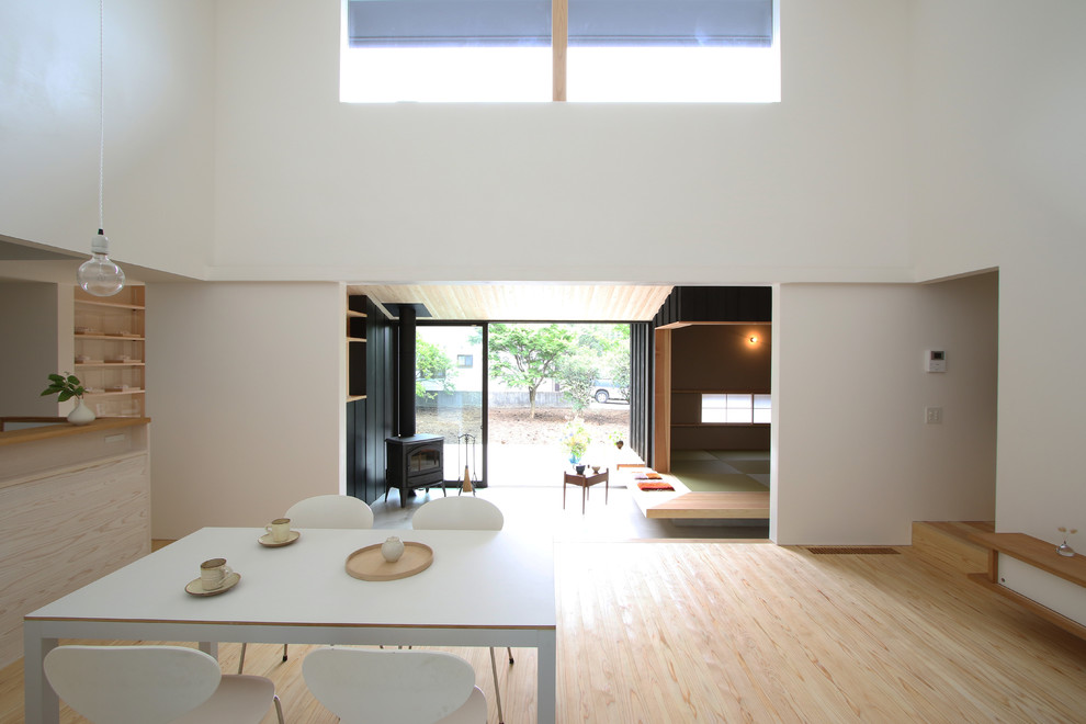 Aménagement d'une salle à manger ouverte sur le salon moderne de taille moyenne avec une cheminée d'angle, un mur blanc, parquet clair, un manteau de cheminée en béton et un sol beige.