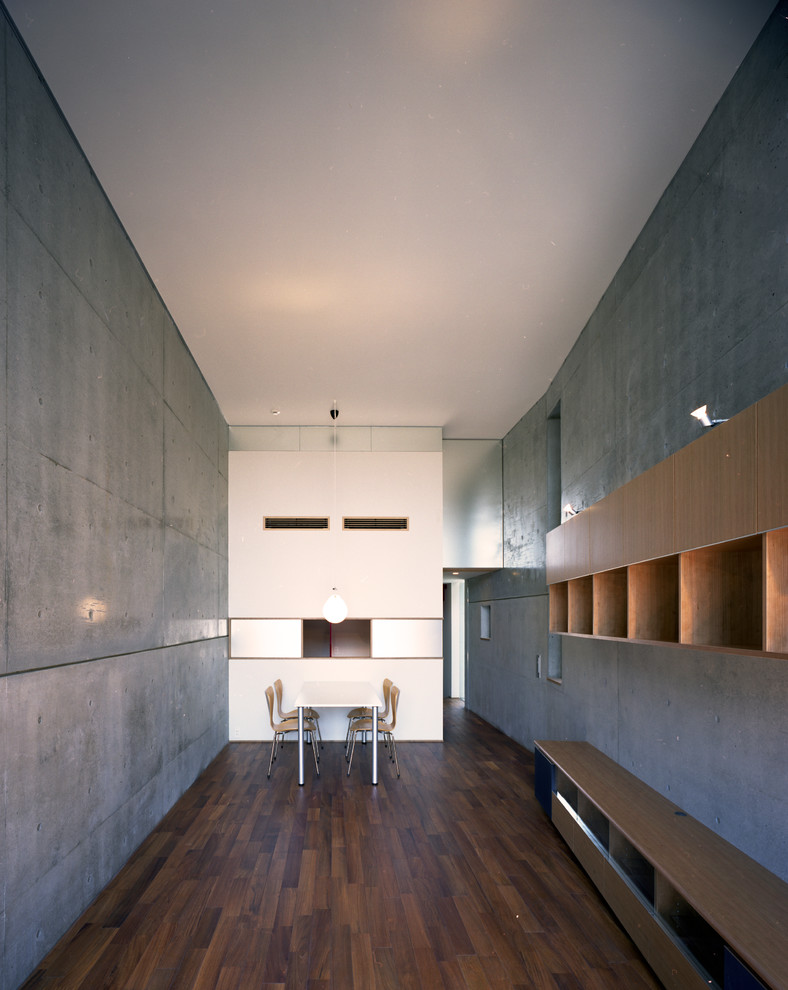 Aménagement d'une salle à manger ouverte sur le salon moderne de taille moyenne avec un mur gris, un sol en bois brun, aucune cheminée, un sol marron et un manteau de cheminée en béton.